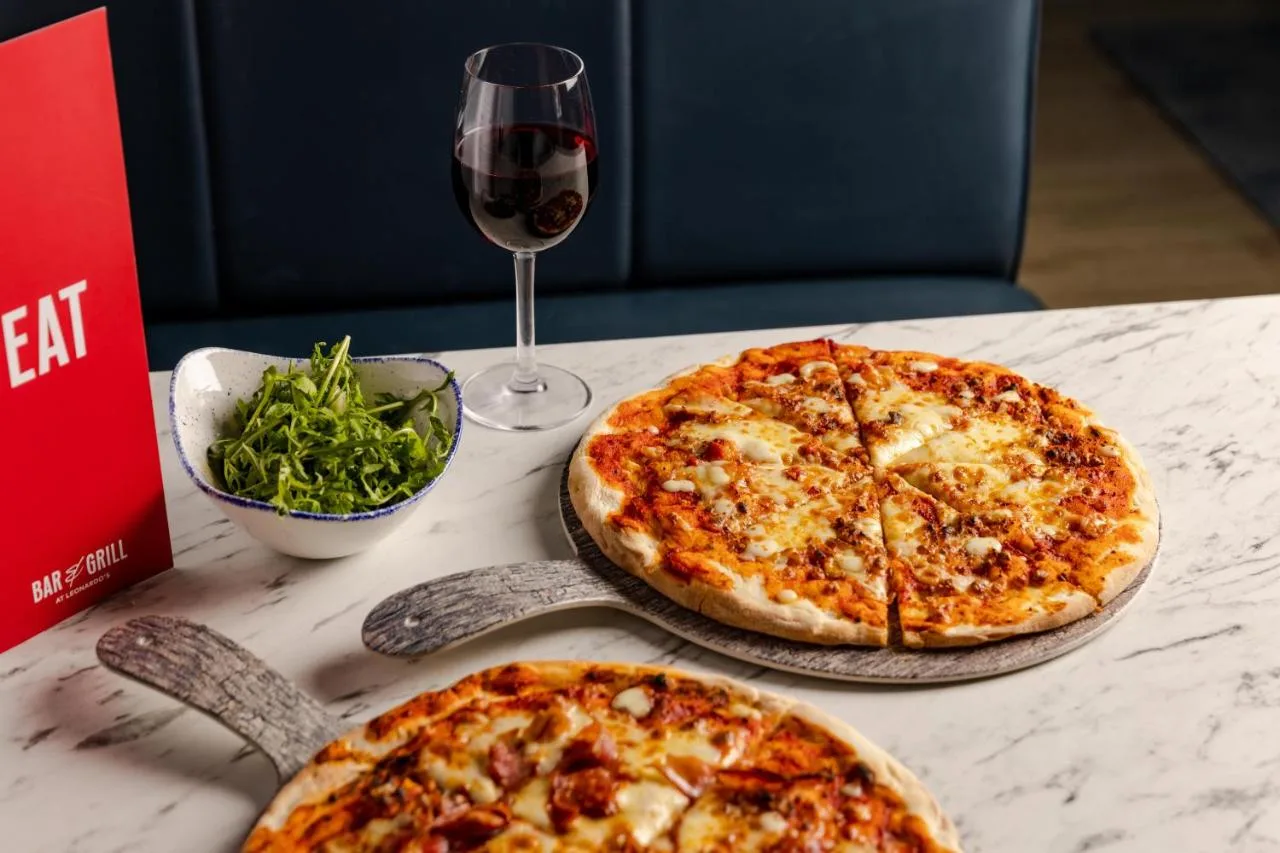two pizzas sitting on a table with a glass of wine at Leonardo Hotel Newcastle in Newcastle upon Tyne