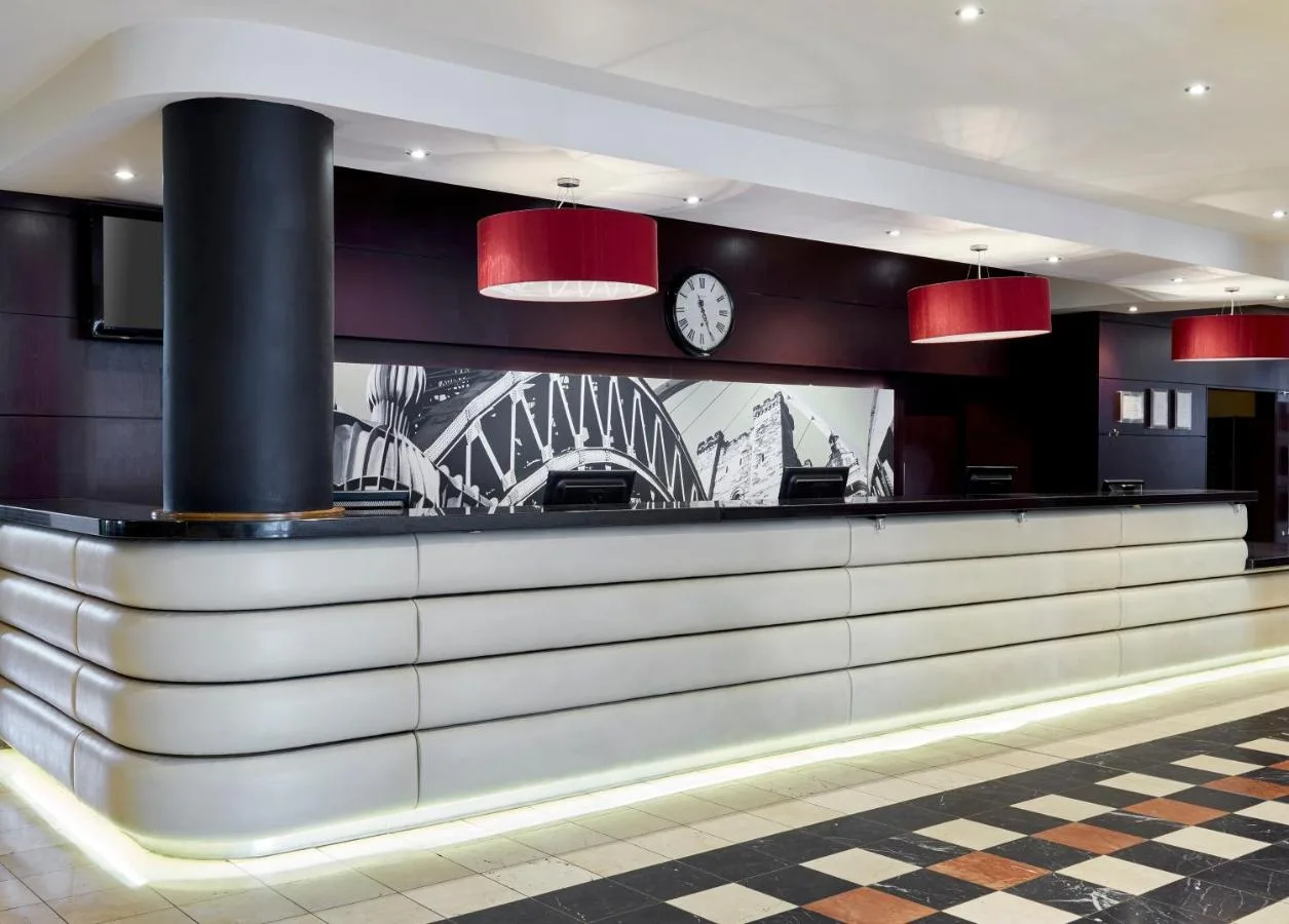 a lobby with a counter with a clock on the wall at Leonardo Hotel Newcastle in Newcastle upon Tyne